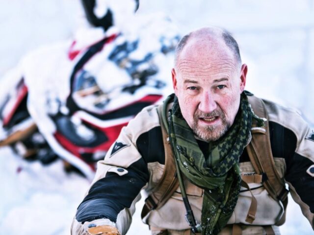 Roland Düringer sitzt im Schnee, hinter ihm liegt seine Africa Twin